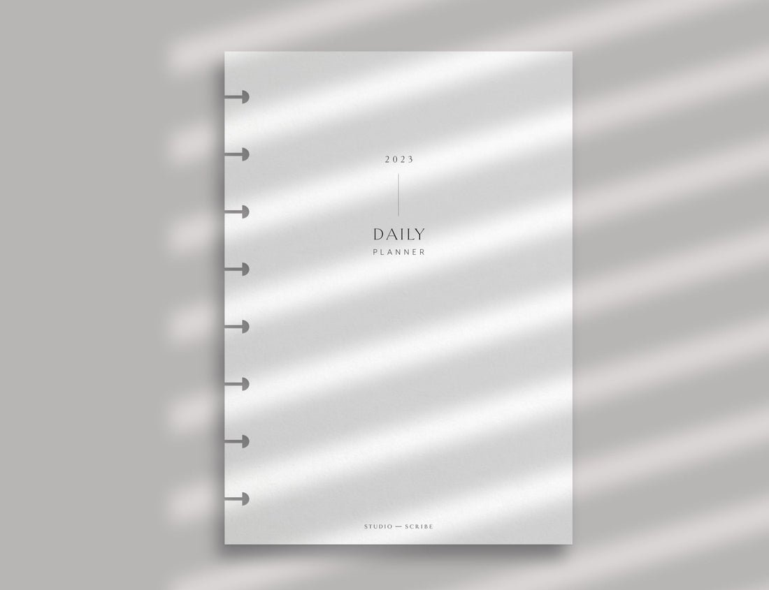 A daily planner page with disc-bound punching set against a soft pink background with shadows from a window blind