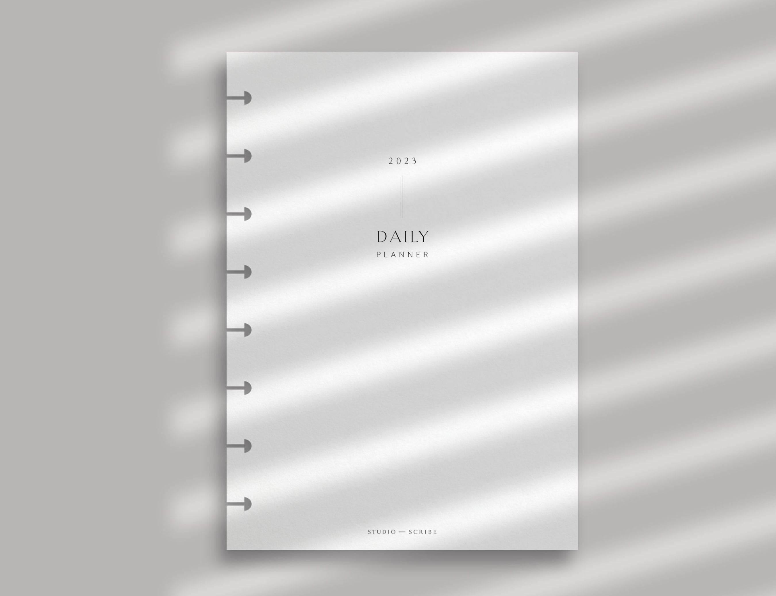 A daily planner page with disc-bound punching set against a soft pink background with shadows from a window blind