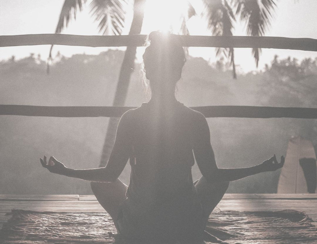 A person meditating on a wooden deck set against a tropical background