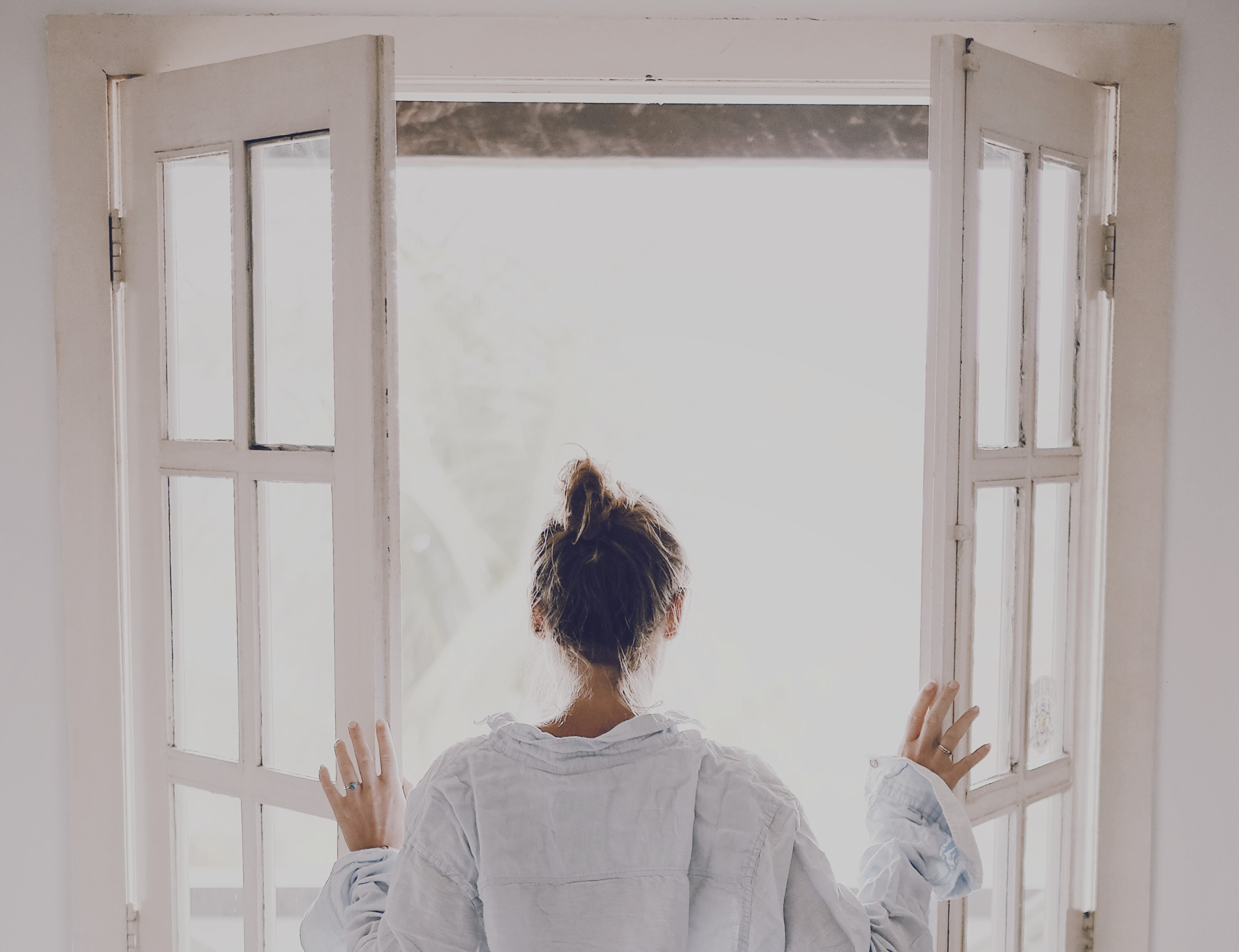 A person opening a set of glass doors to look outside to the sunshine