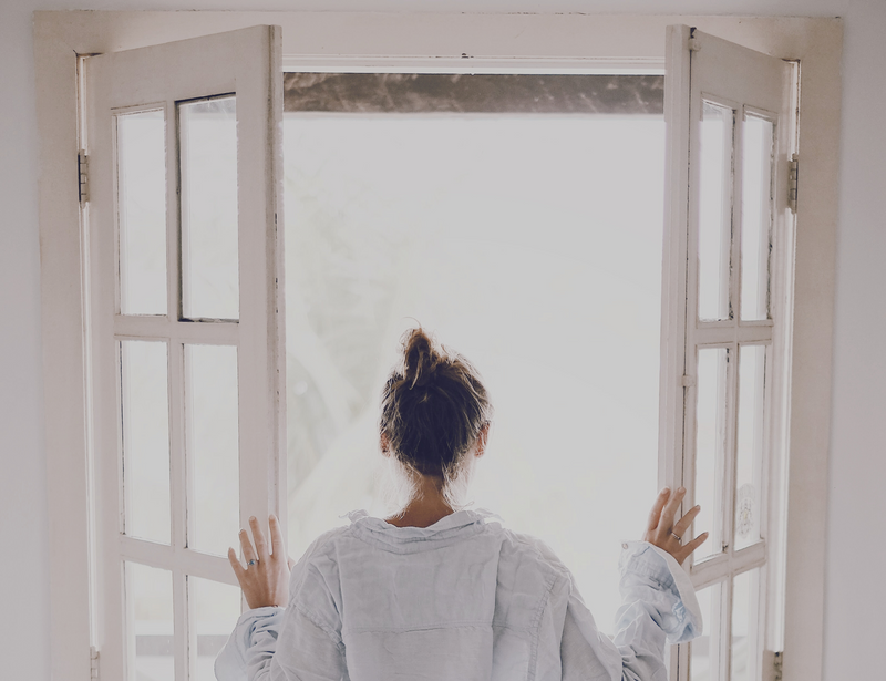 A person opening a set of glass doors to look outside to the sunshine