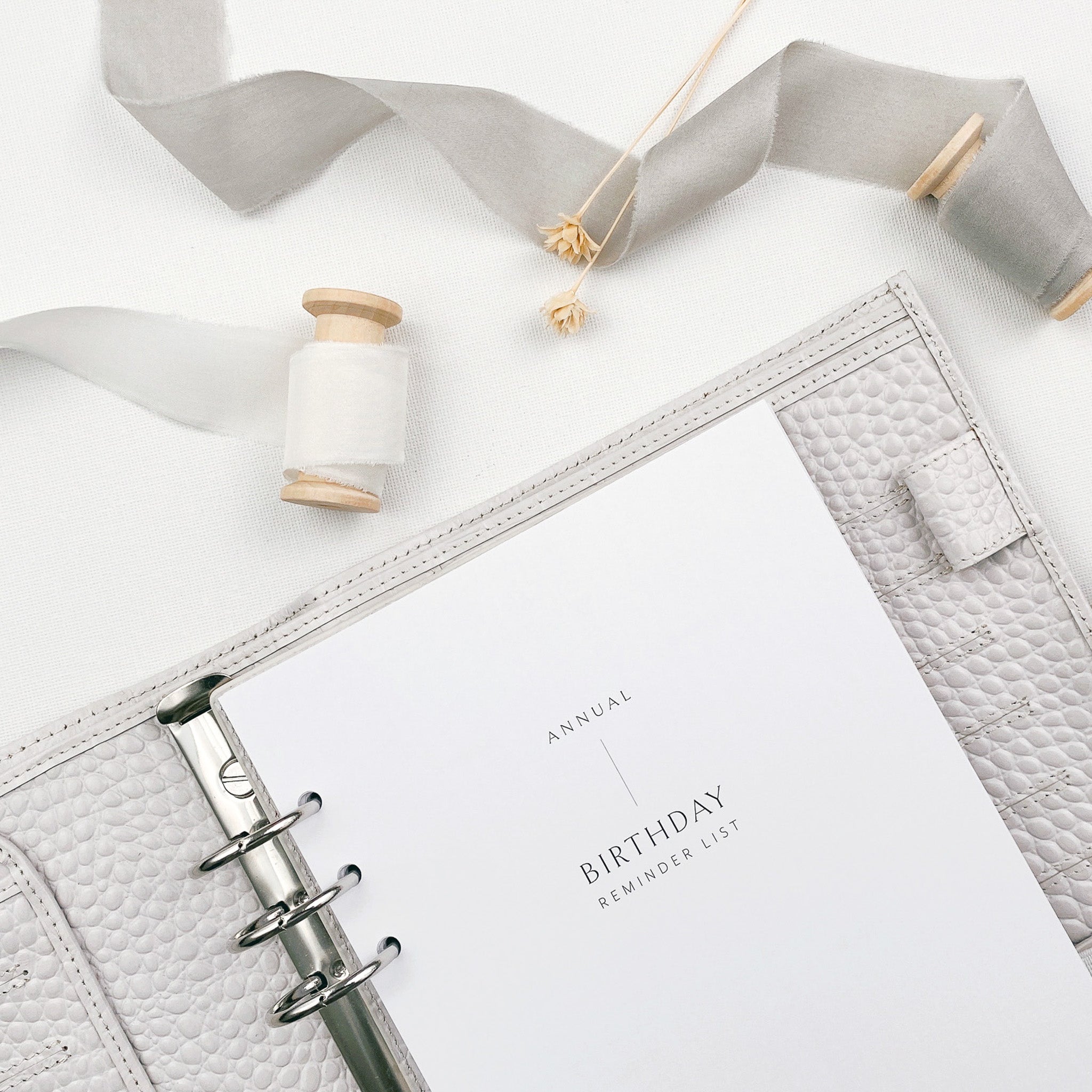 Printed birthday reminder list pages in an open planner on a white background