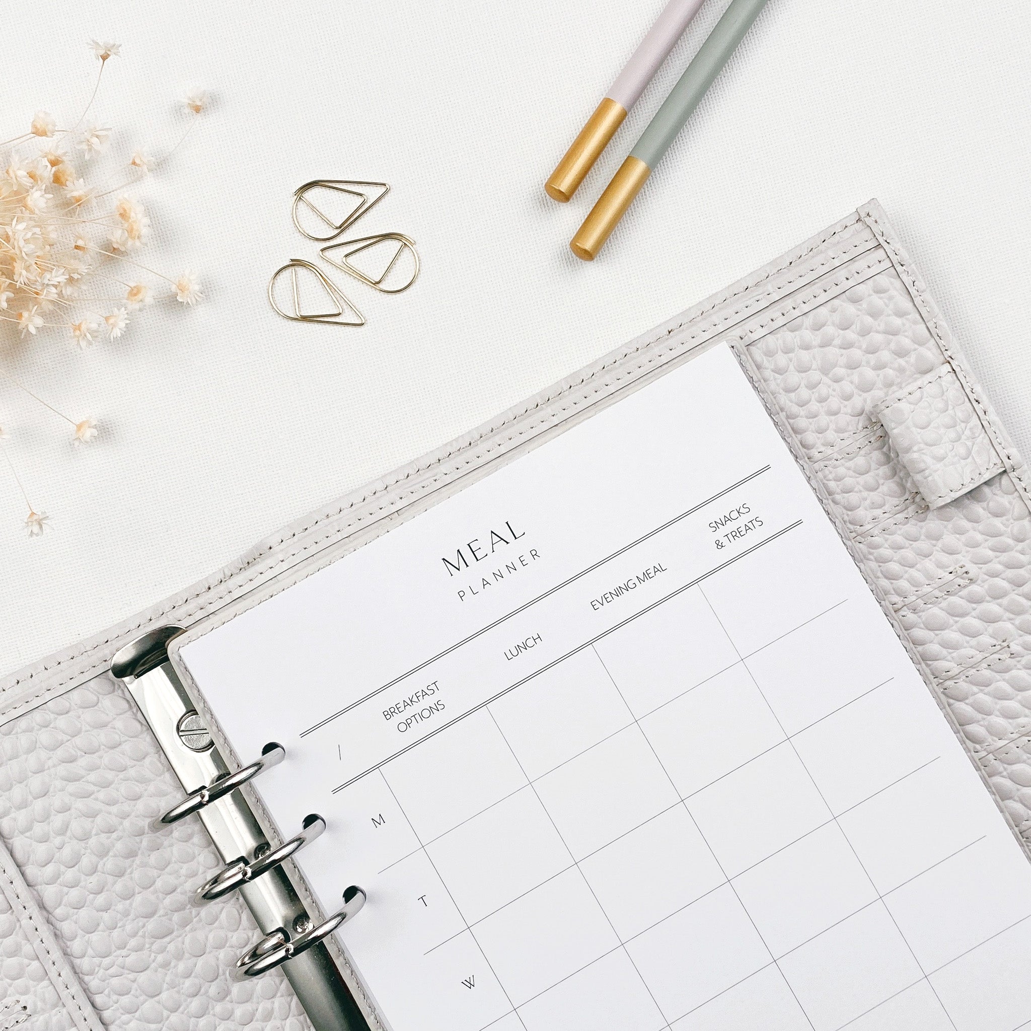 A meal planner page shown in an open planner, laying on a white surface with pencils and paperclips nearby
