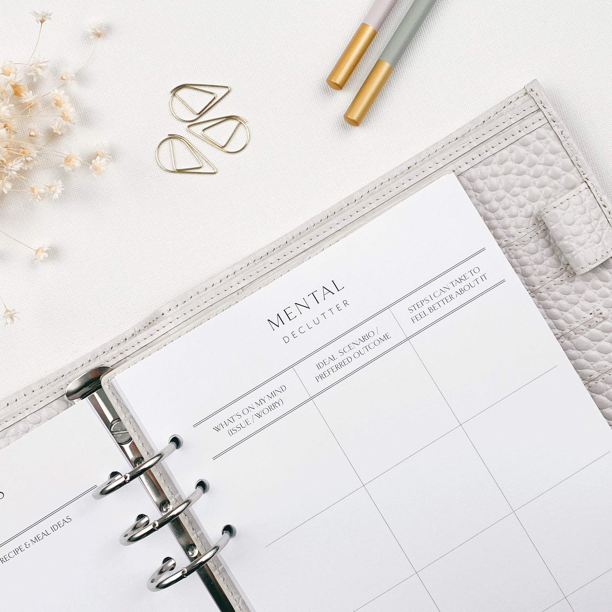 A personal organiser open to a 'mental declutter' planner page with a light background and stationery items nearby