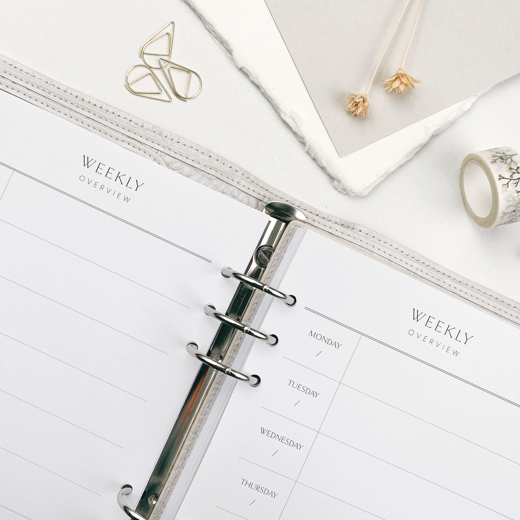 An open planner with 2 weeks to view against a light surface with decorative items nearby