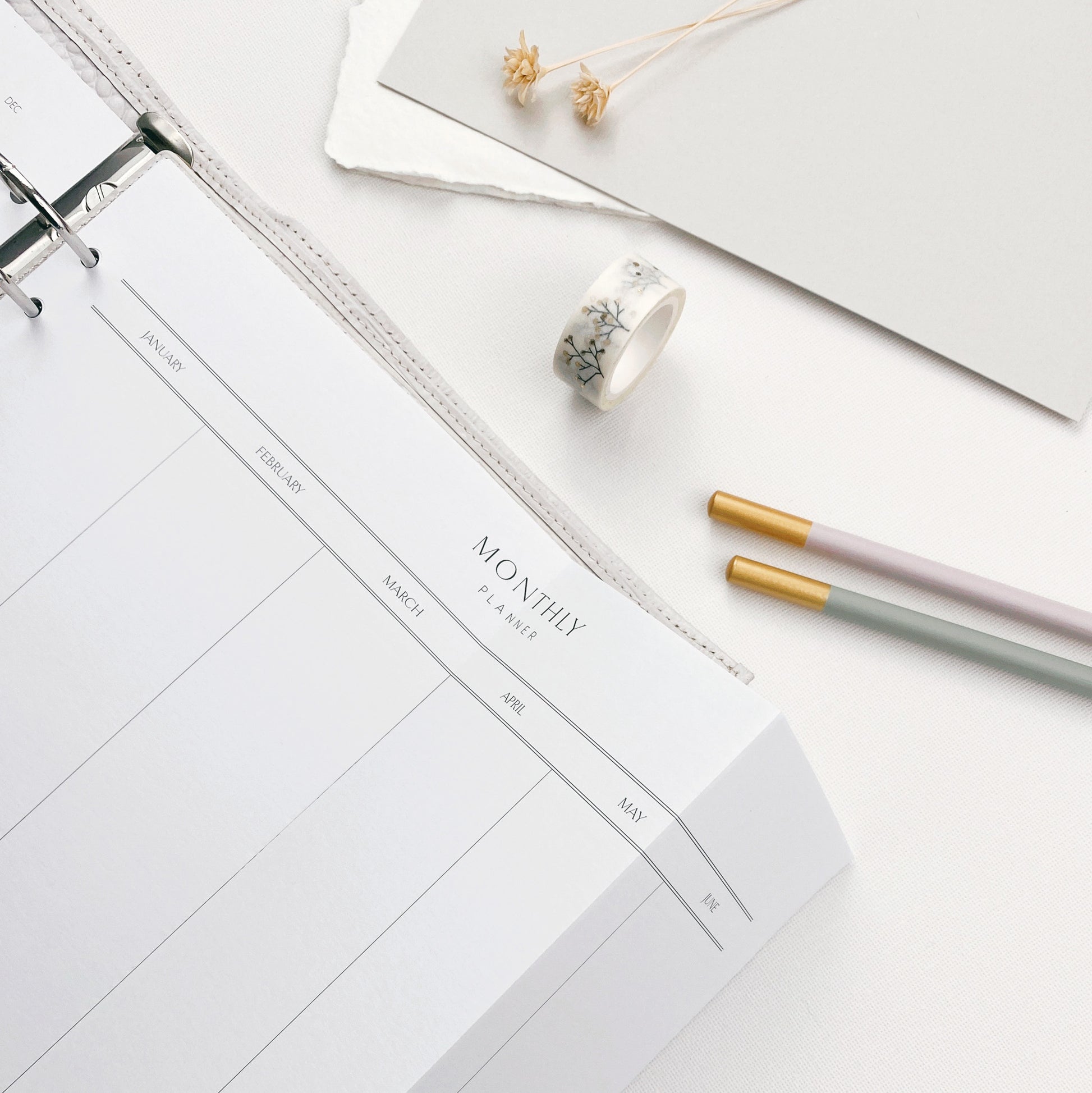 Printed A4 landscape planner page, folded to fit an A5 organiser, surrounded by various stationery items.