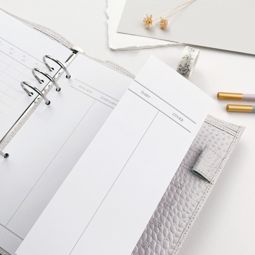 Printed A4 landscape planner page, folded to fit an A5 organiser, surrounded by various stationery items.