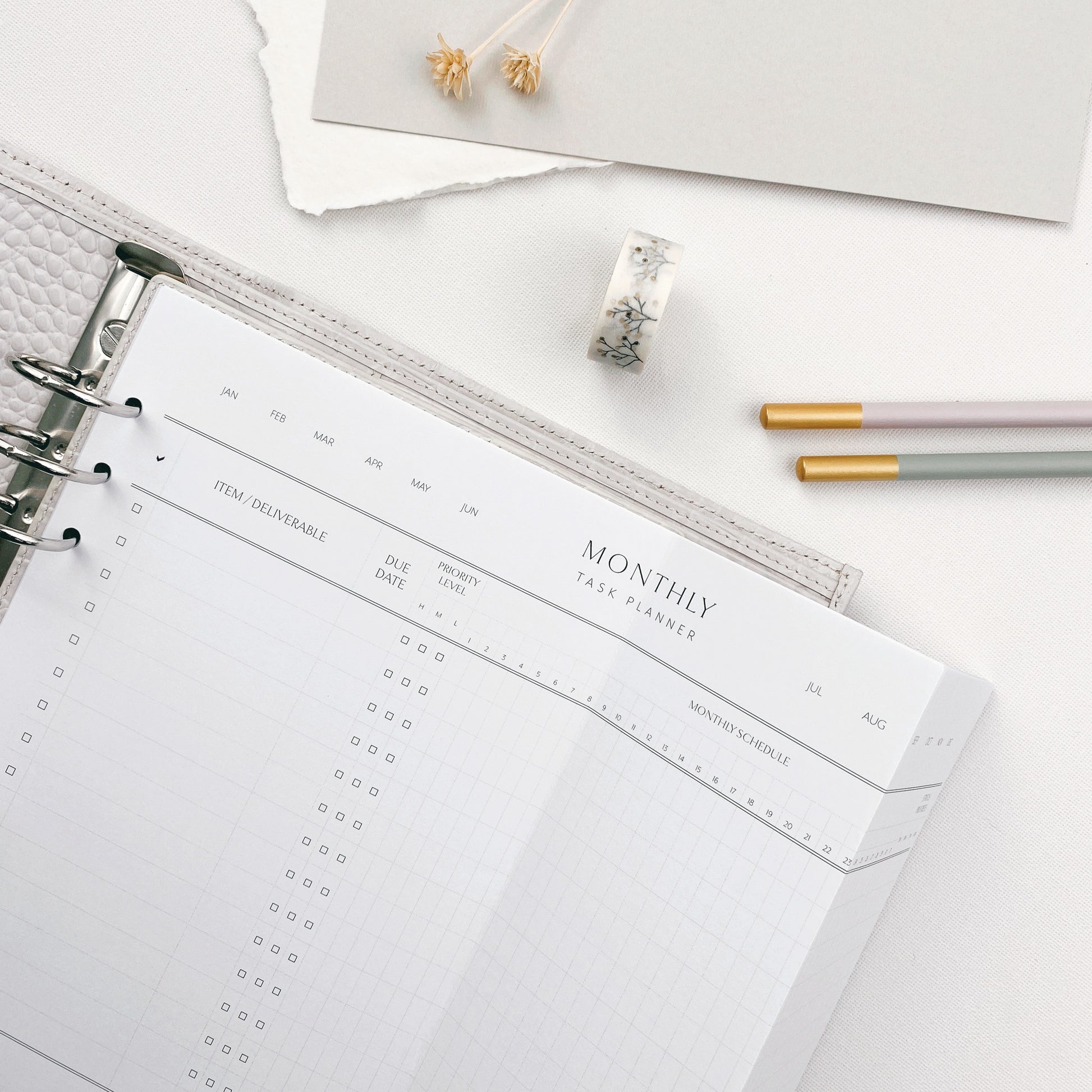 A4 printed landscape page with a monthly task planner design, folded to fit an A5 organiser and surrounded by stationery items