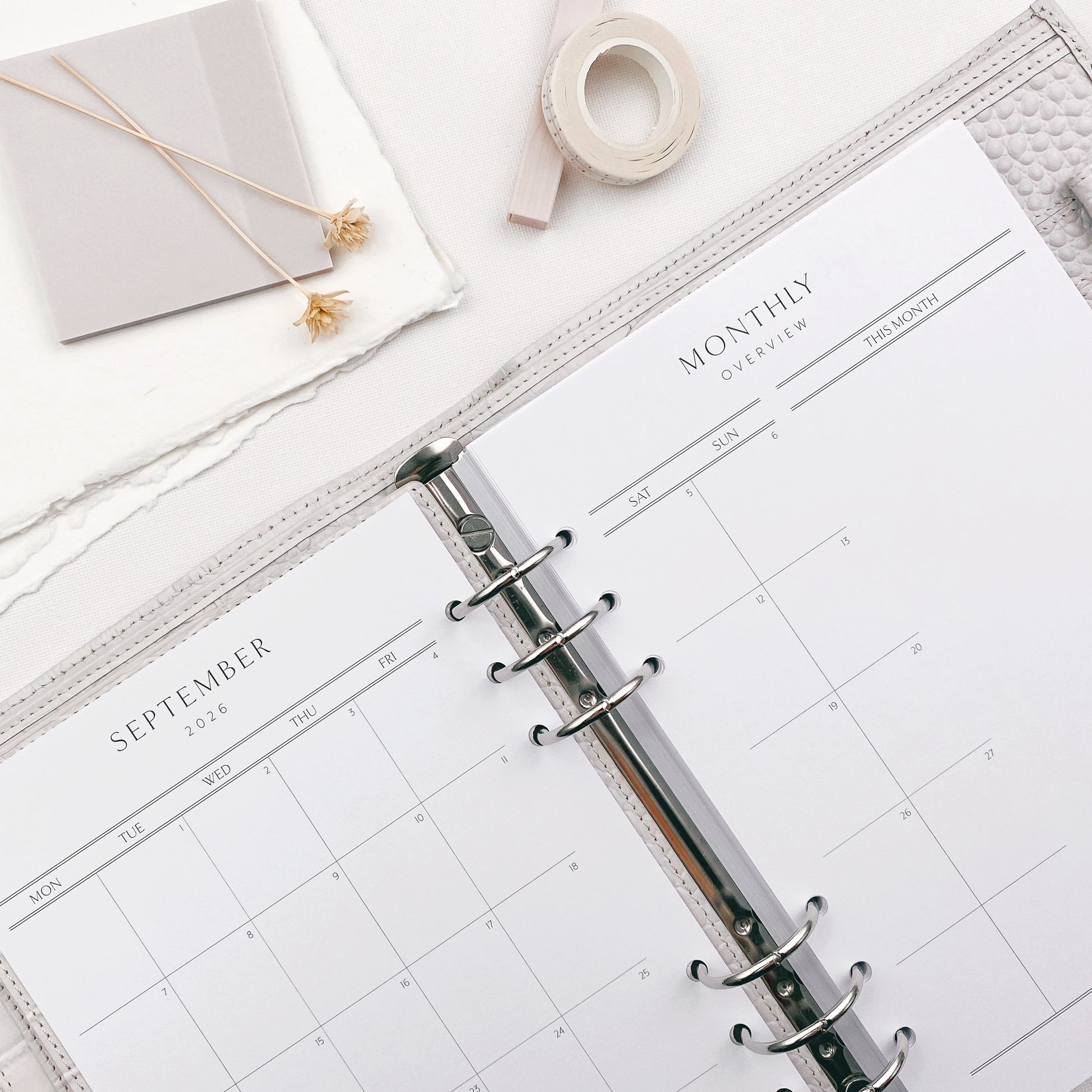 Open planner with monthly overview on a white surface, featuring a pen and tape.