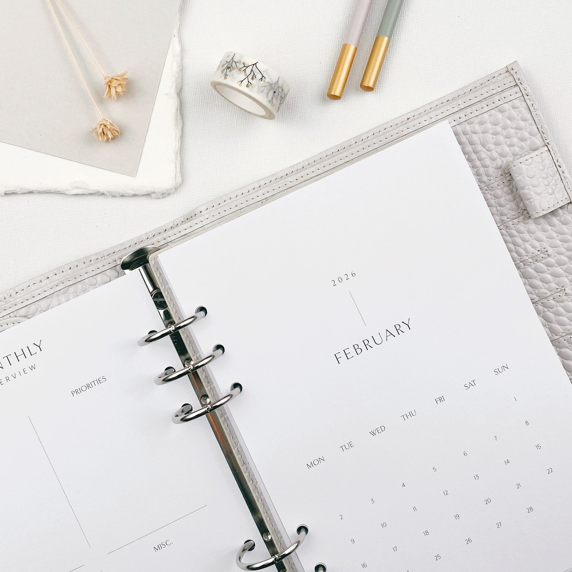Open planner with monthly calendar page on a white surface with stationery items.