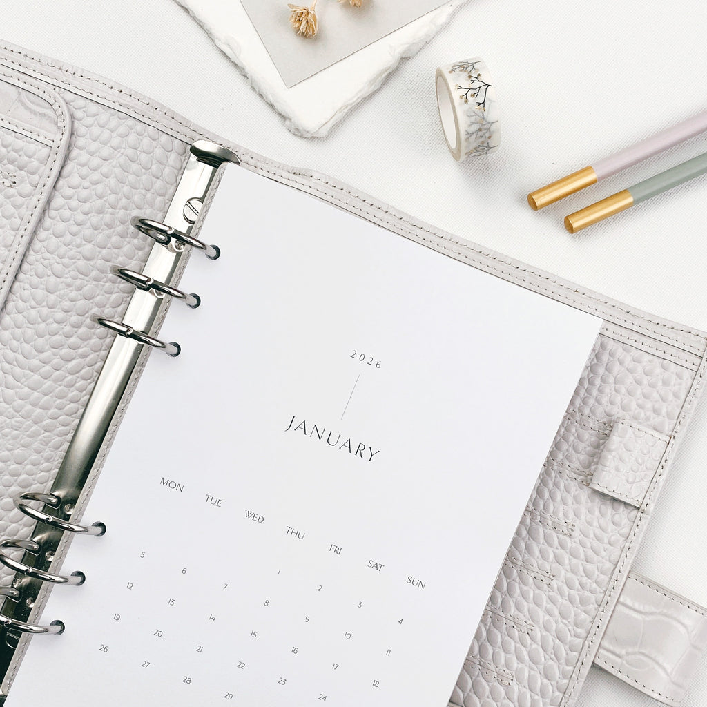 Open planner with monthly calendar on a white surface with gold tipped pencils and washi tape.