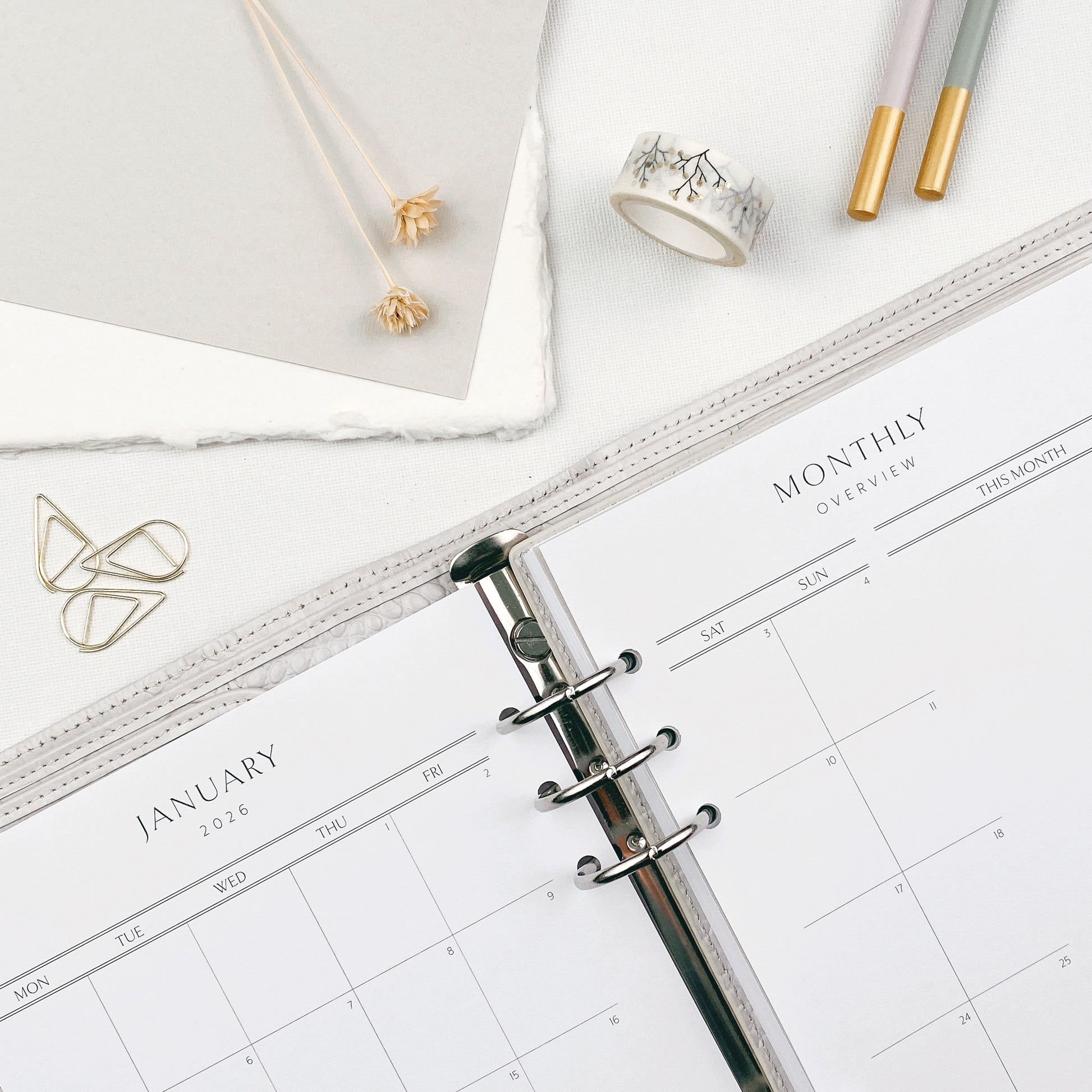 Planner open to monthly calendar pages on a light surface with decorative and stationery.
