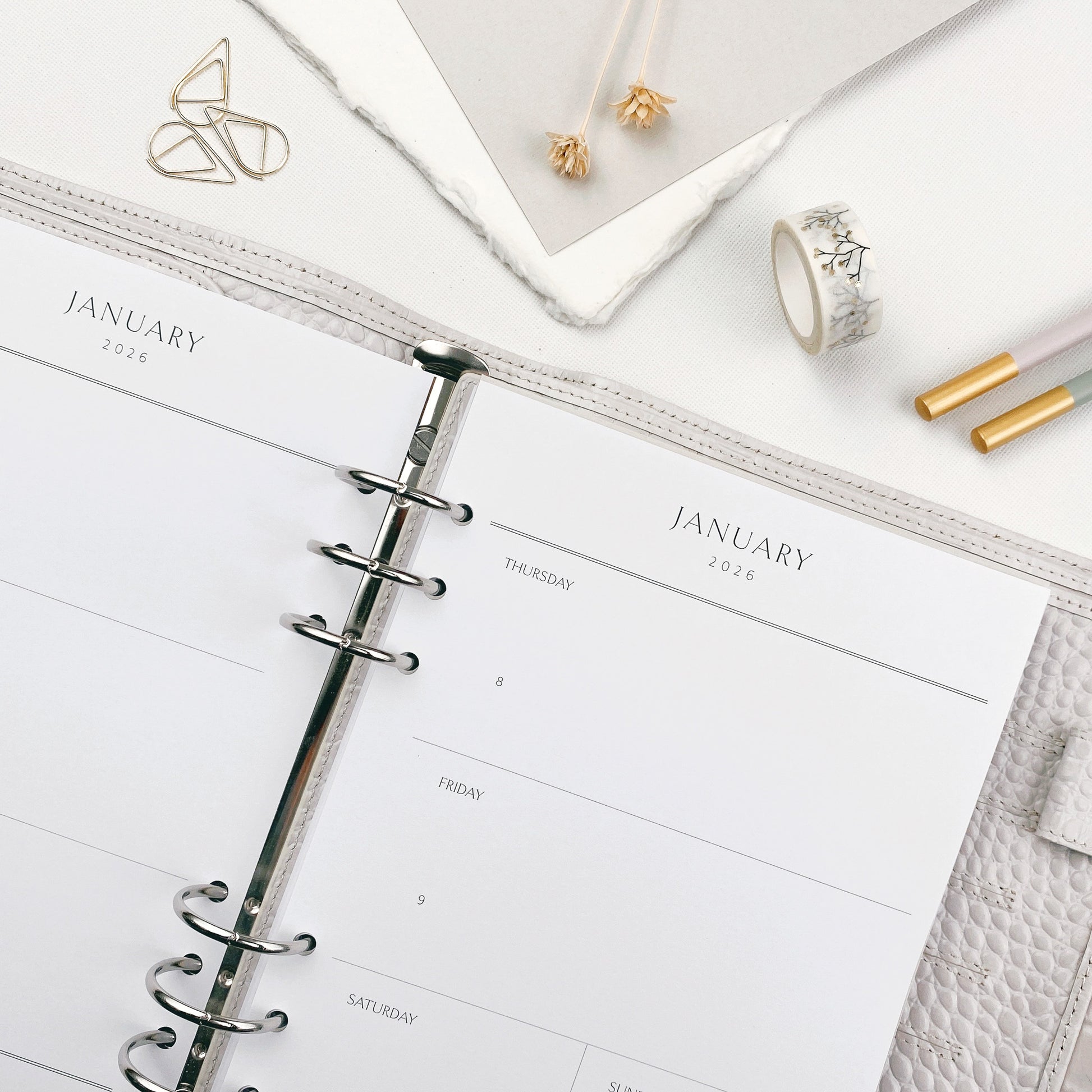 Weekly planner open to January with stationery items on a white surface