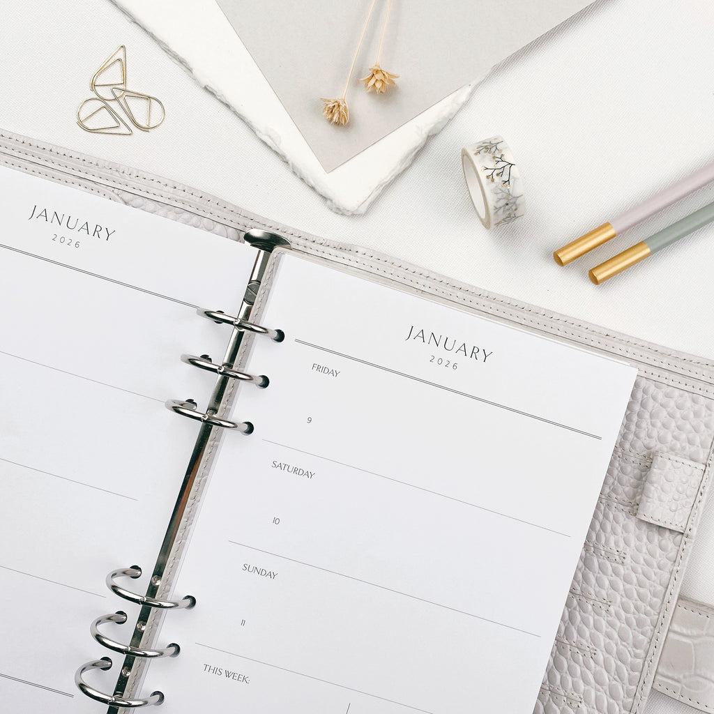Open planner with weekly classic overview layout on a white surface with gold stationery accessories.
