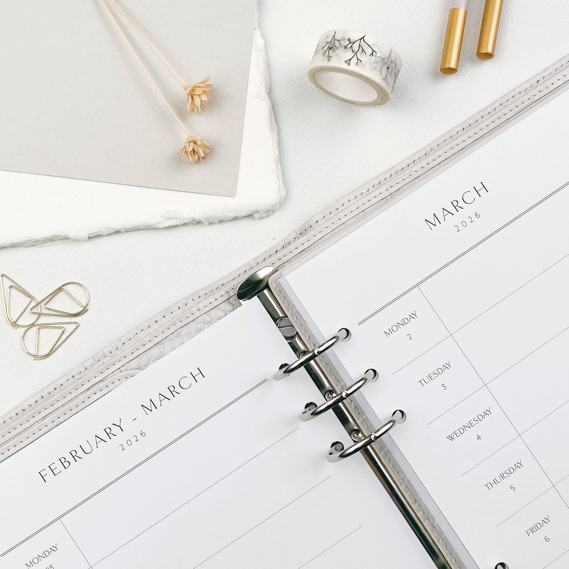 Weekly planner open to March 2026 with stationery items on a white surface