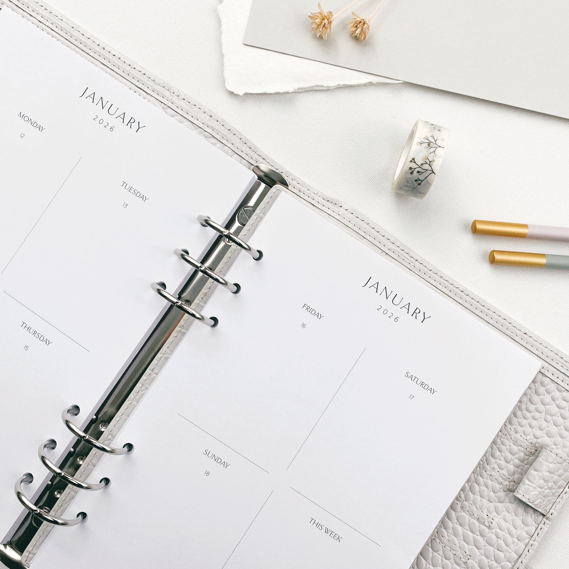 Open planner with weekly pages on a white surface with stationery items.