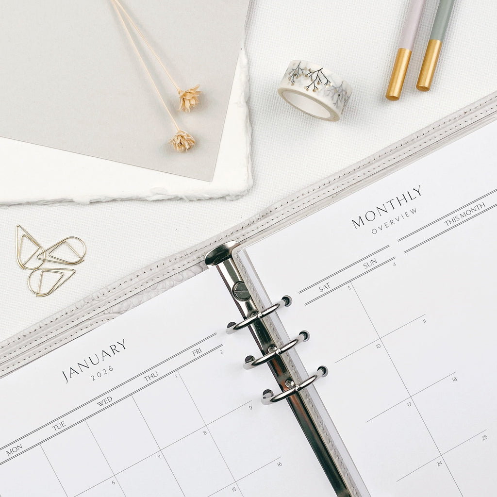 Planner with monthly grids on a white surface with decorative and stationery items.