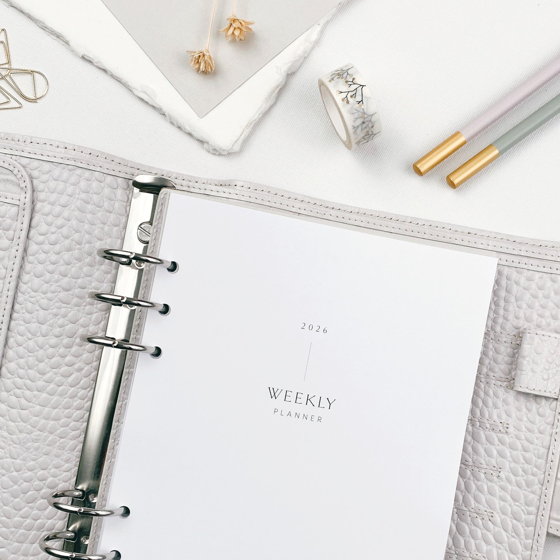 Weekly planner pages in a grey organiser and decorative items on a light surface.
