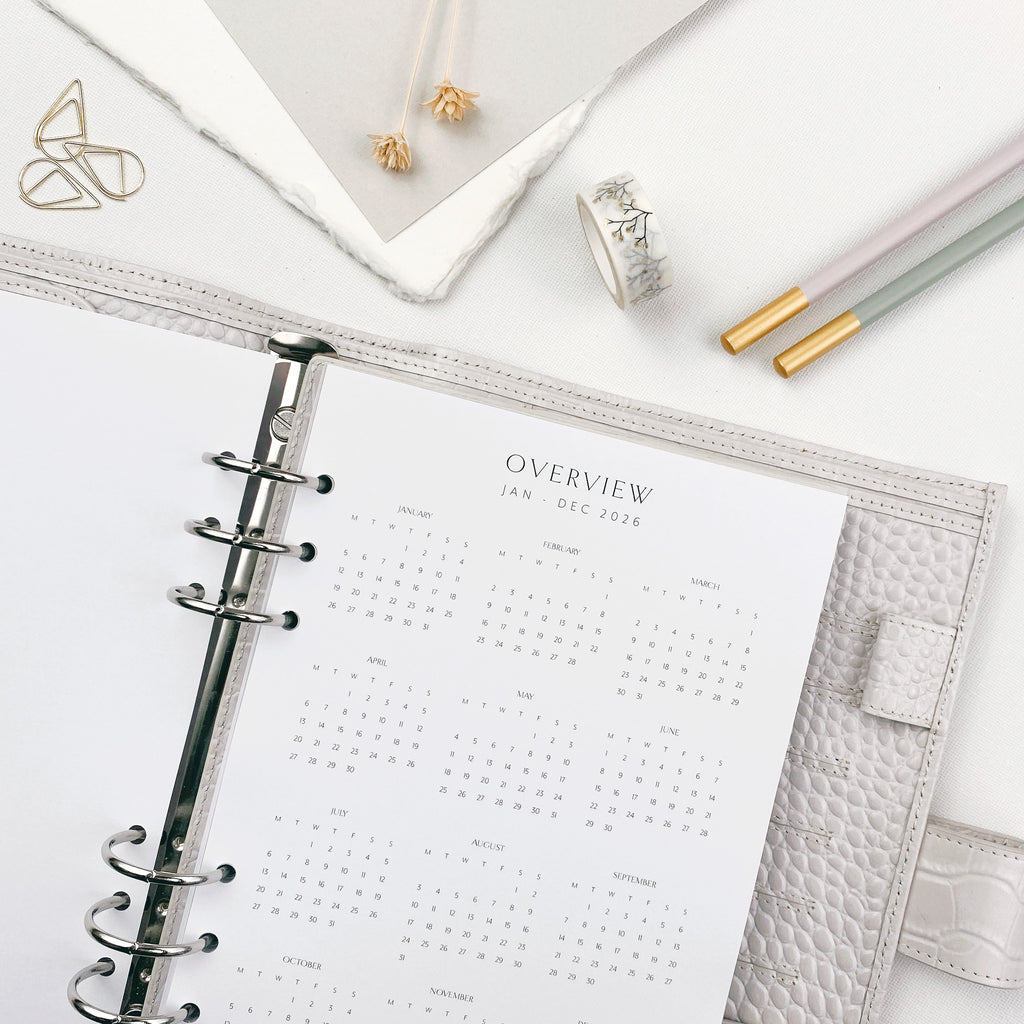 Open personal organiser with yearly calendar page on a white surface with stationery items.