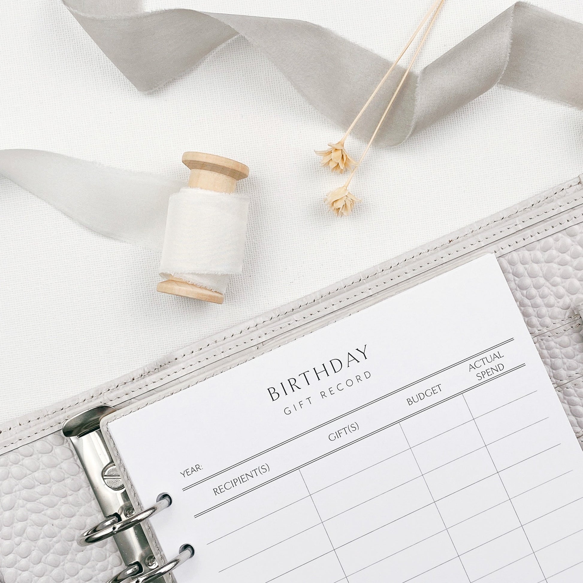 Personal organiser with a birthday gift record planner page on a white surface with decorative items.