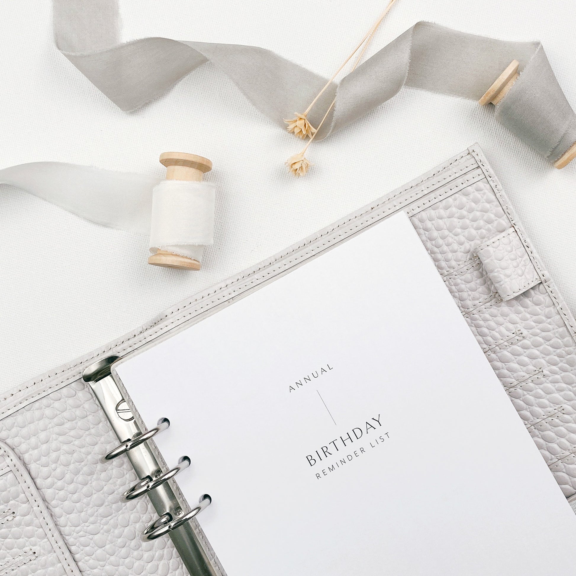 Planner with 'Annual Birthday Reminder List' on a white surface with decorative elements.
