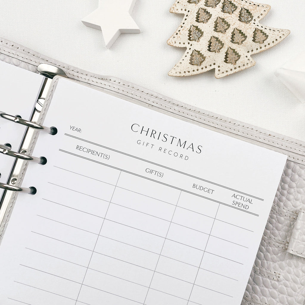 Christmas gift record planner sheet on a white surface with decorative items.