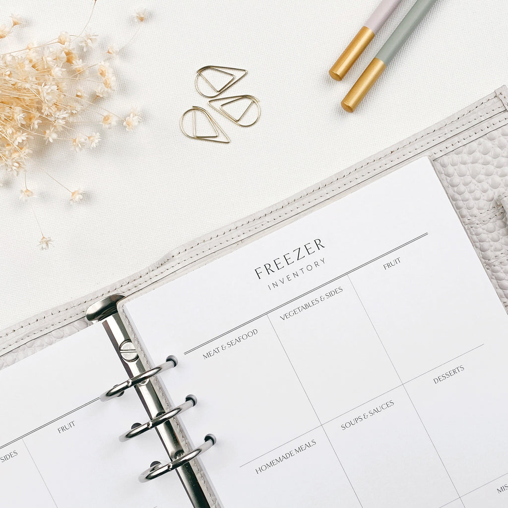 Open planner with 'Freezer Inventory' section on a light surface with decorative elements.