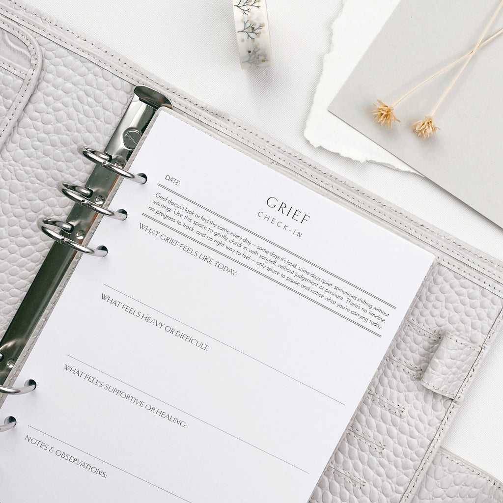 Grey planner with a page titled 'Grief Check-In' on a white surface.