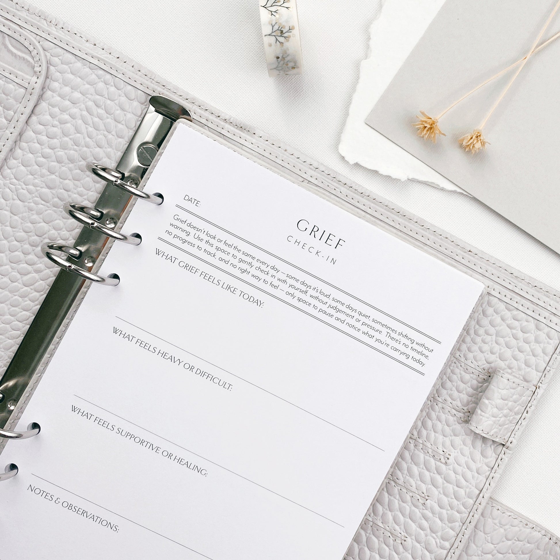 Grey planner with a page titled 'Grief Check-In' on a white surface.