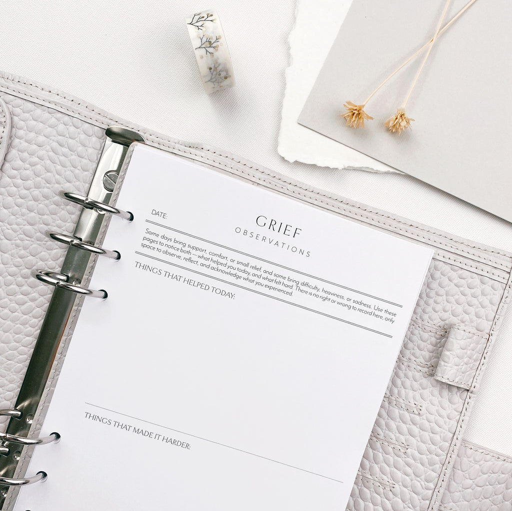 Open planner with a page titled 'Grief Observations' on a white surface.