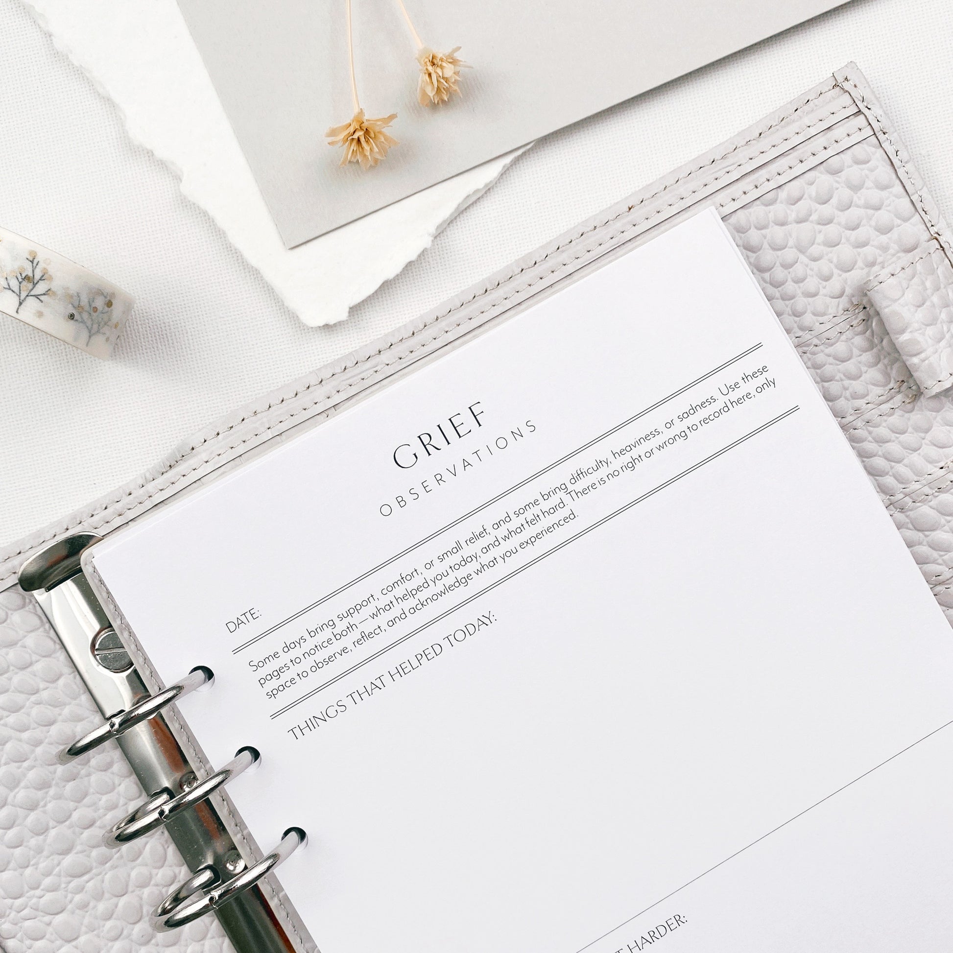 Open planner with a page titled 'Grief Observations' on a white surface.