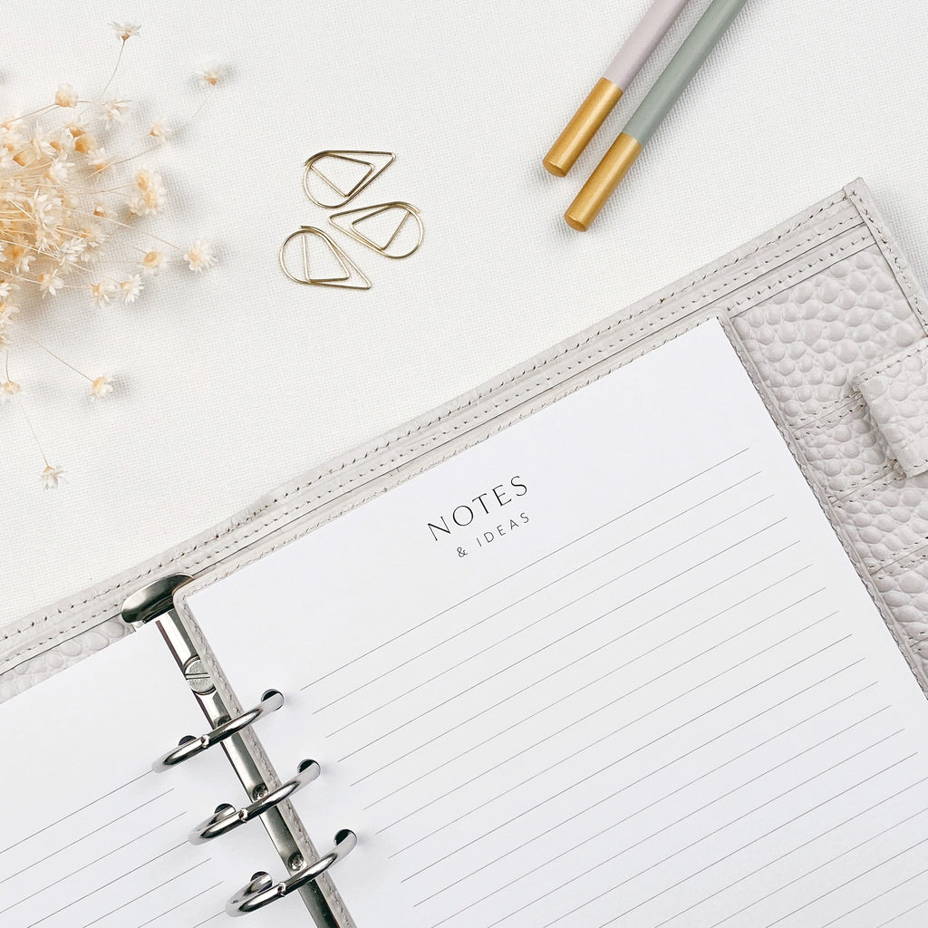 Open planner with 'Notes & Ideas' page on a white surface with decorative elements.