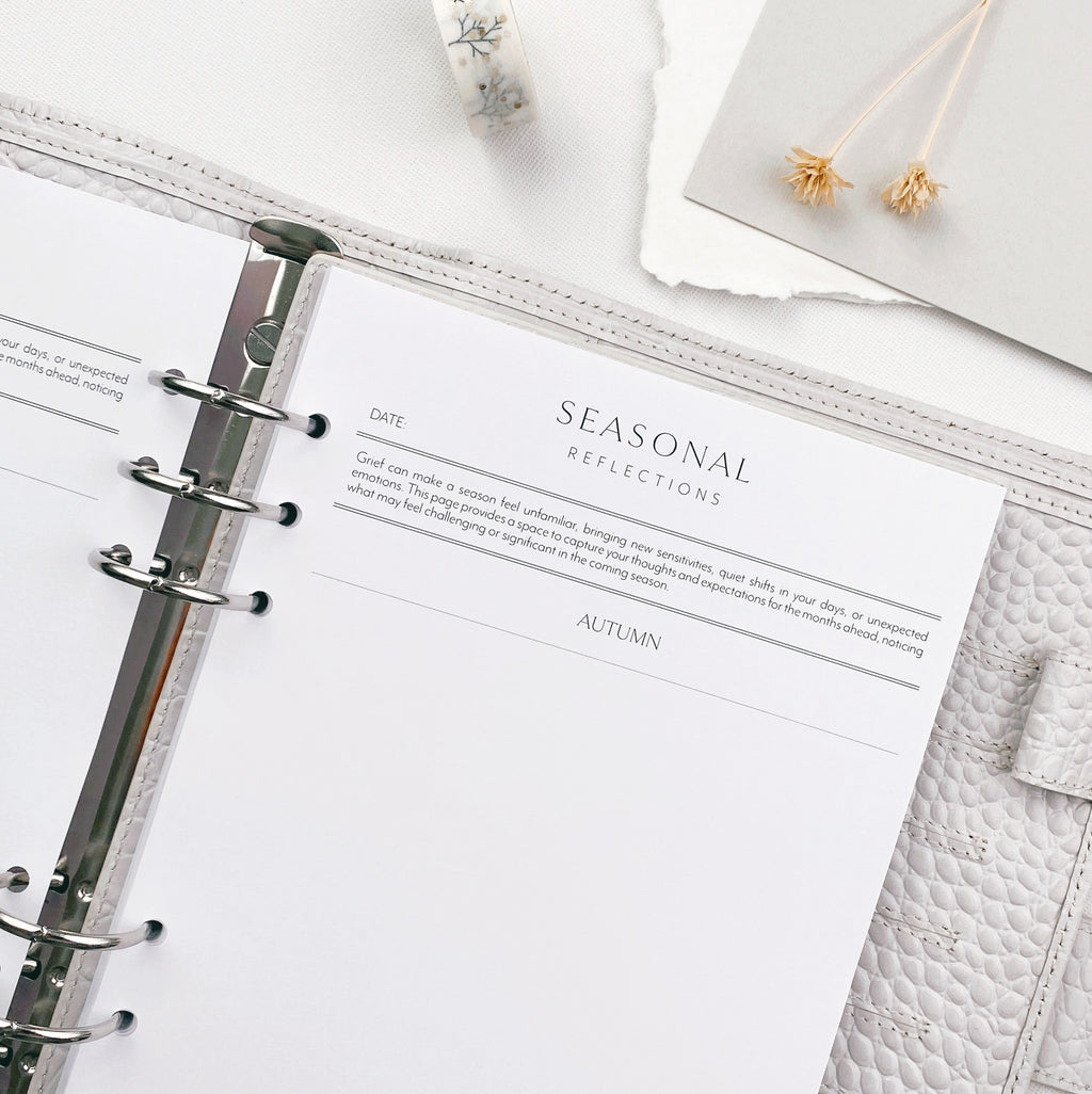 Open planner with 'Seasonal Reflections' page on a white surface with decorative elements.