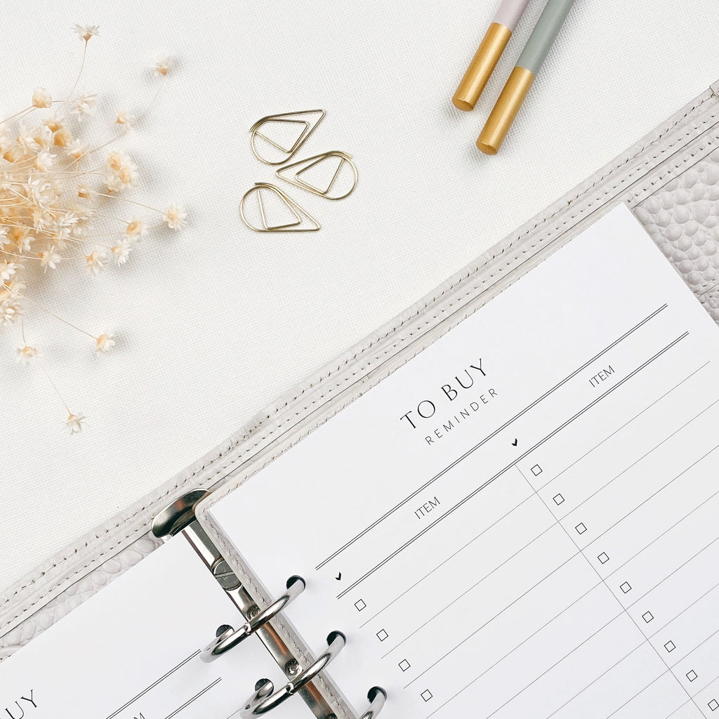 Open planner with 'To Buy' reminder section on a white surface with decorative elements.