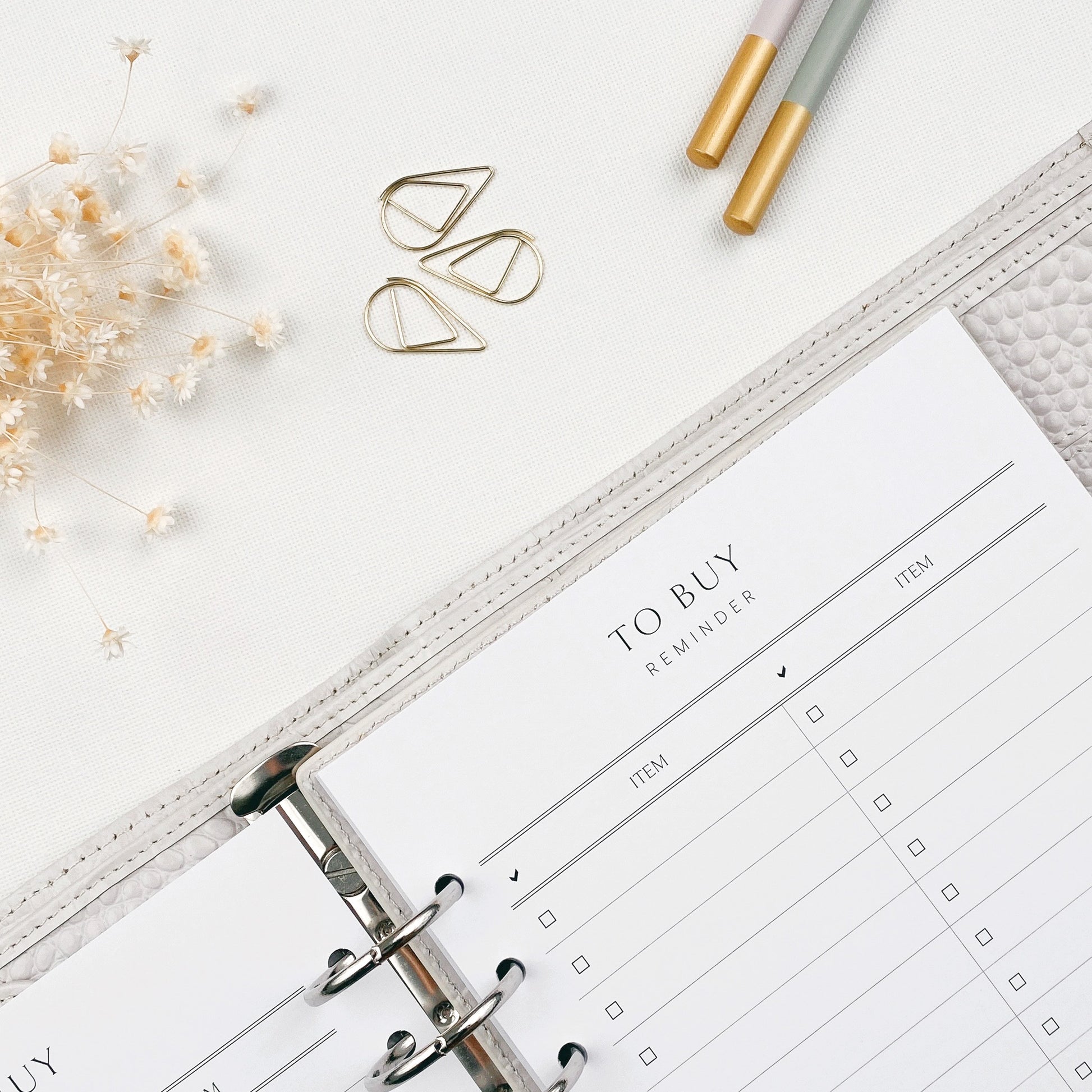Open planner with 'To Buy' reminder section on a white surface with decorative elements.