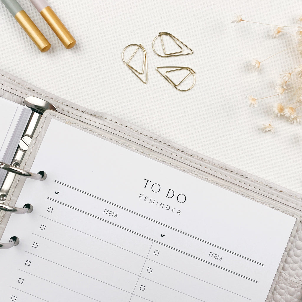 Open planner with 'To Do Reminder' page, gold paper clips, and decorative elements on a light surface.