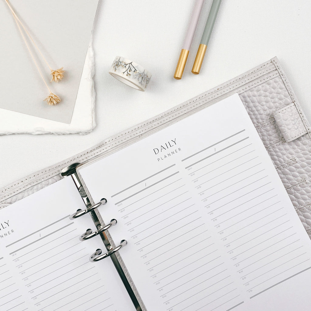 Open daily planner on a light surface surrounded by stationery items.