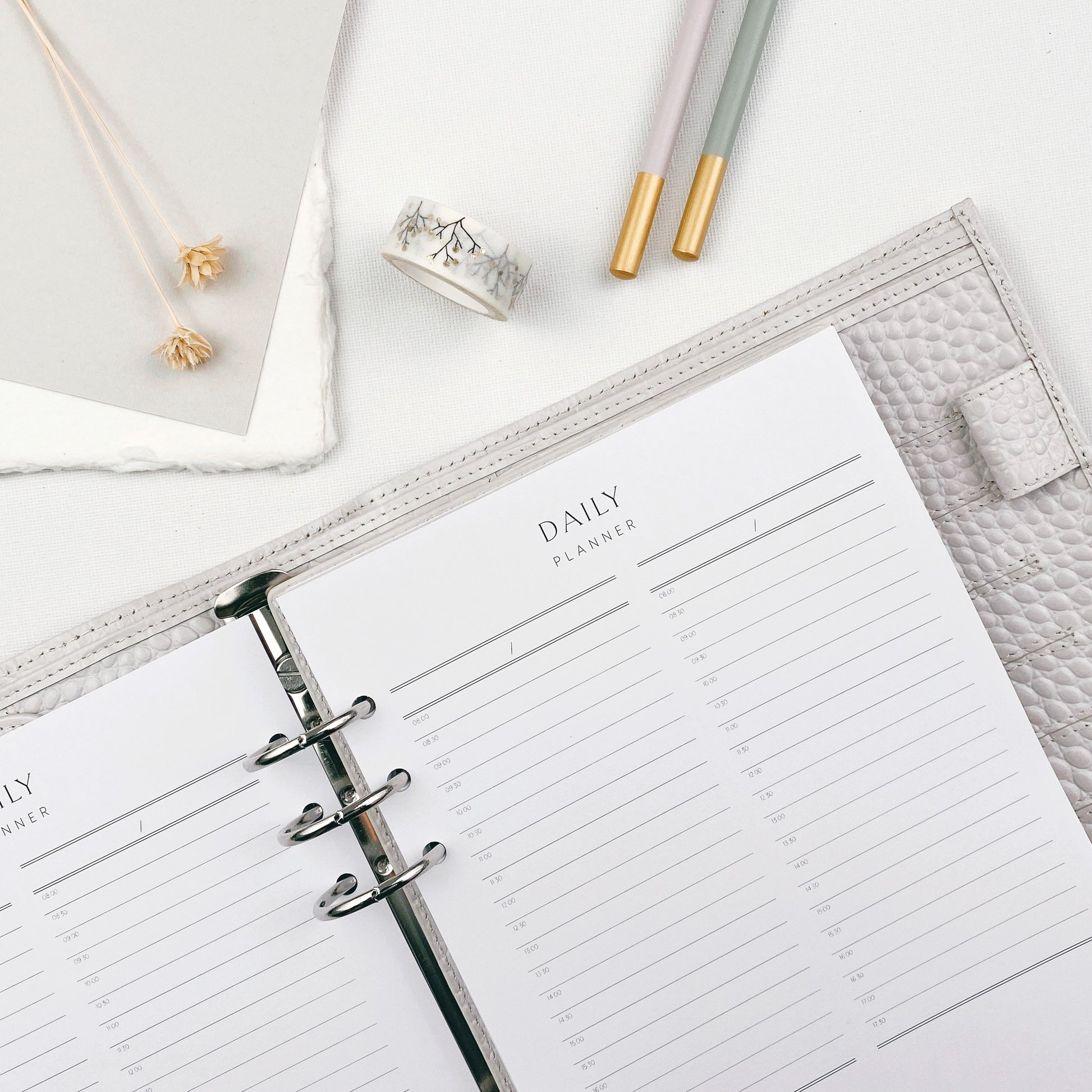 Open daily planner on a light surface surrounded by stationery items.