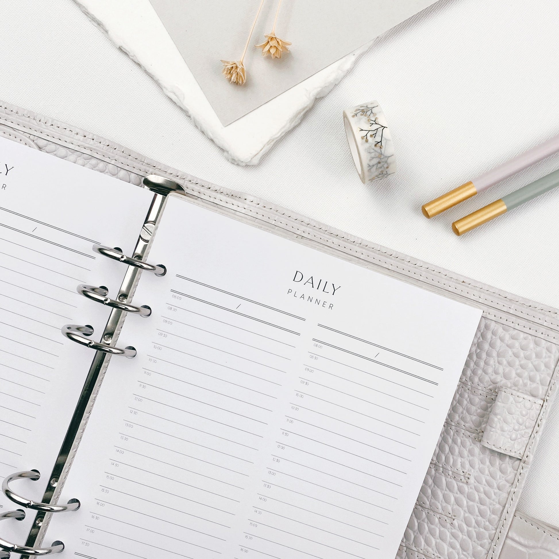 Daily planner with pencils and stationery items on a white surface