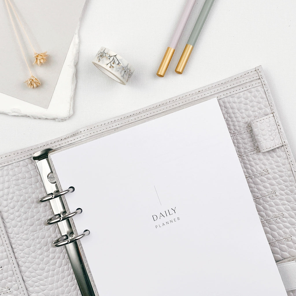 Undated daily planner refills in an organiser on a light surface, surrounded by stationery items.