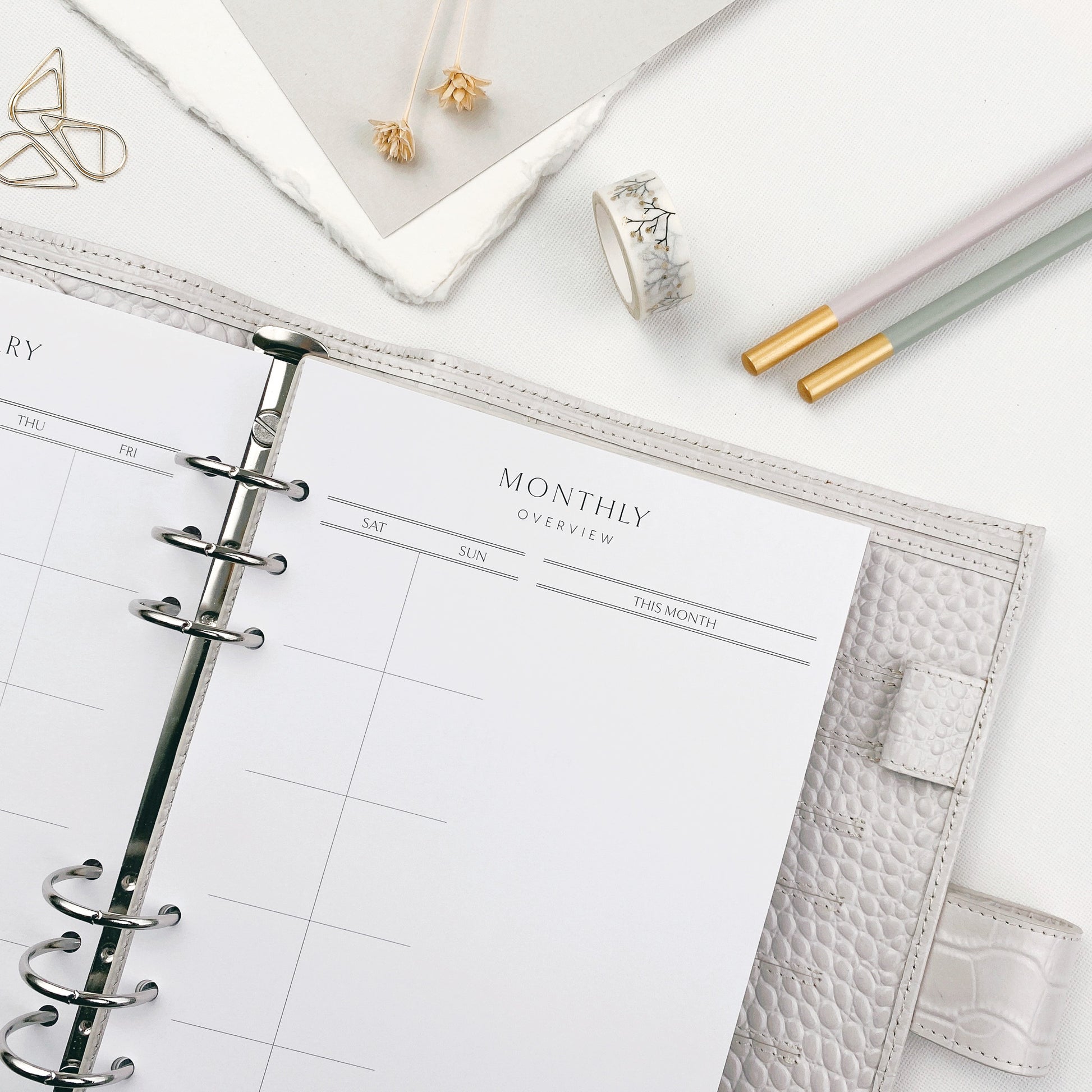 Open planner with monthly overview on a white surface with decorative items.
