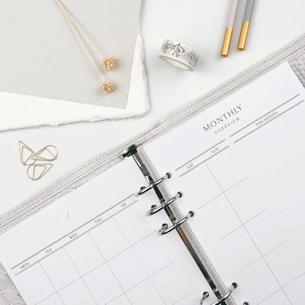 Open planner with monthly overview on a white surface with stationery items.