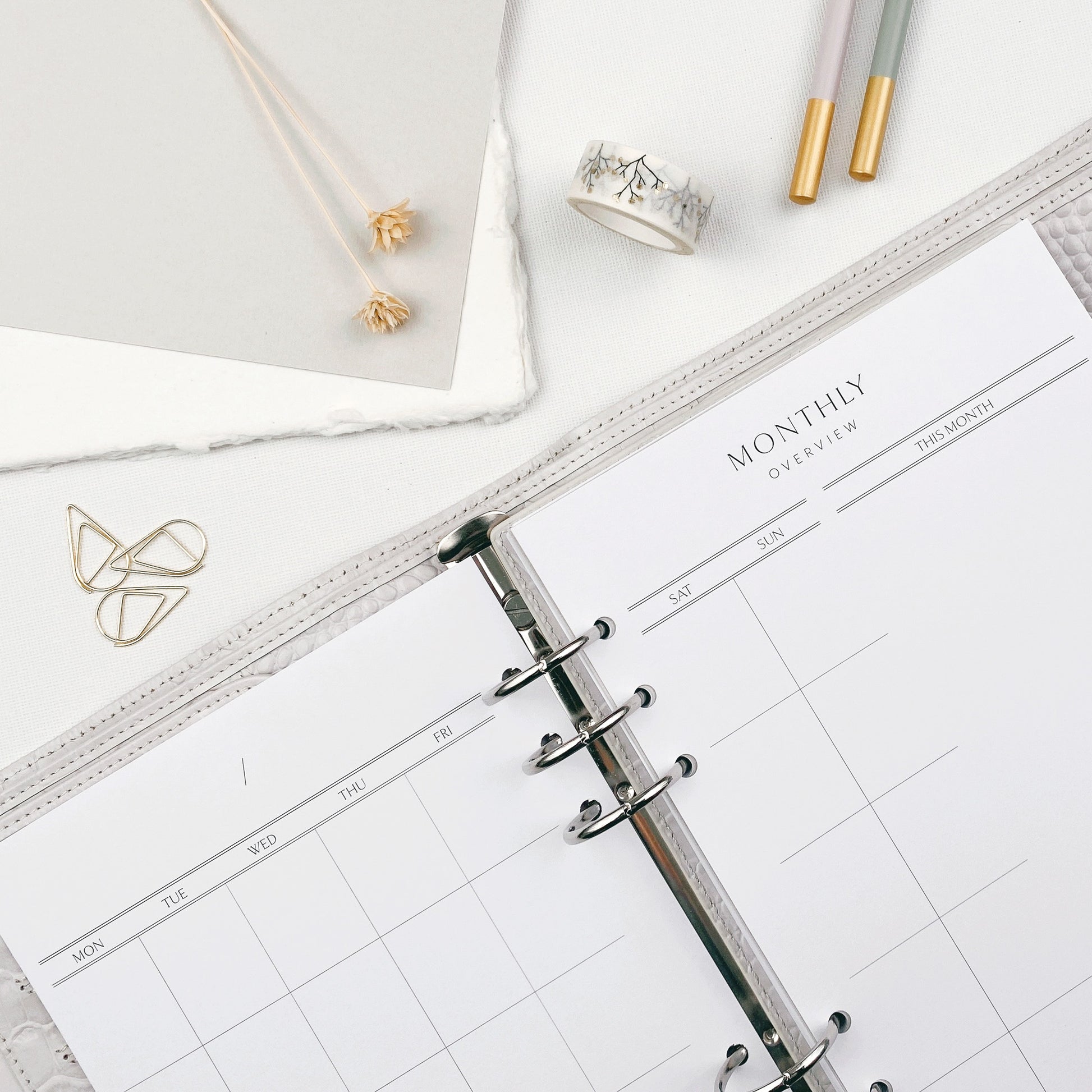 Open planner with monthly overview on a white surface with stationery items.