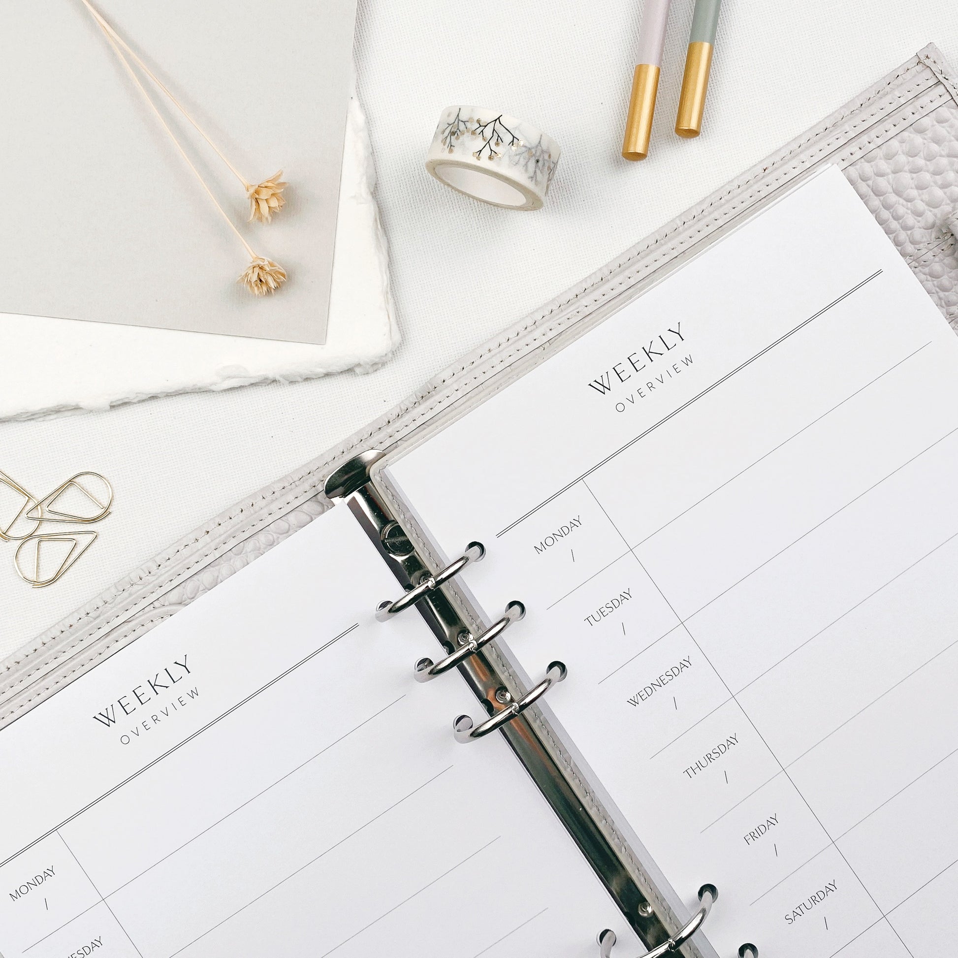 Open planner with weekly overview on a white surface, featuring pencils and small decorative items.