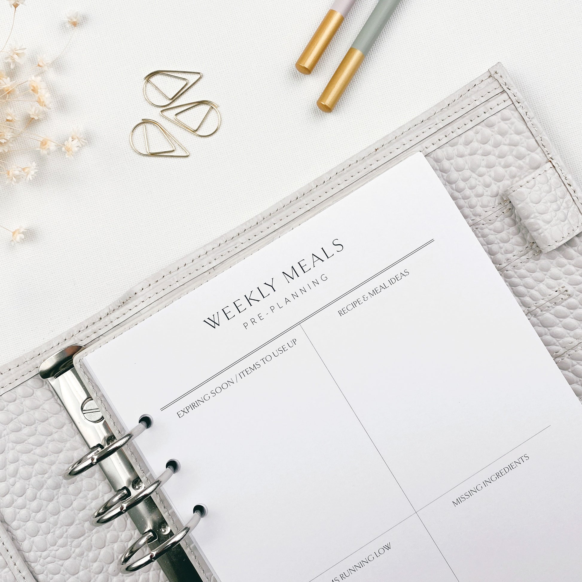Weekly meals planner with pencils and decorative items on a white surface