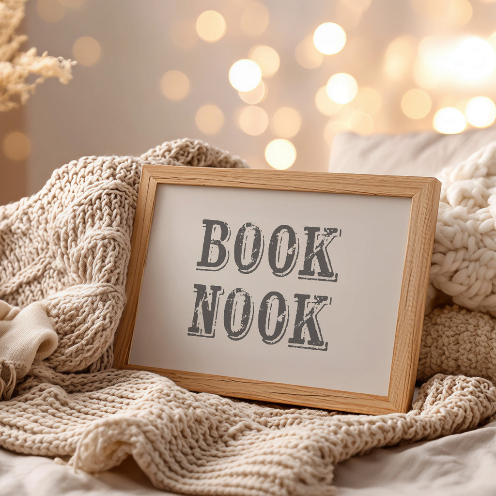 Framed art print with 'BOOK NOOK' text on a cozy blanket with blurred lights in the background