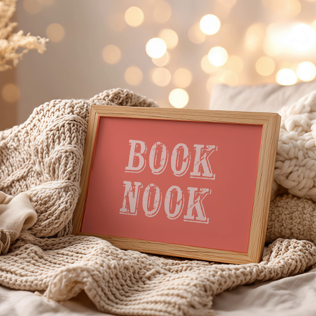 Framed art print with 'BOOK NOOK' text on a cozy blanket with blurred lights in the background