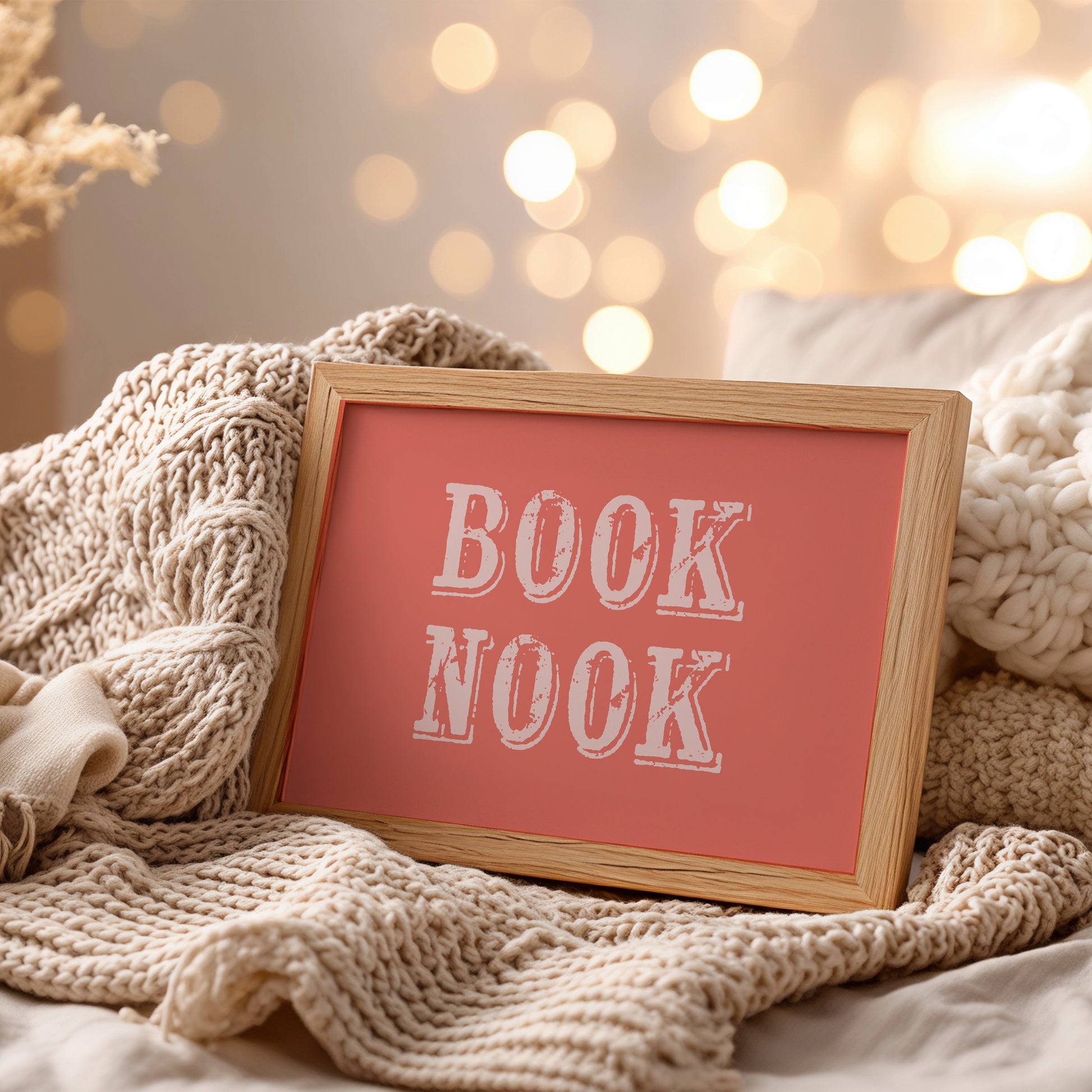 Framed art print with 'BOOK NOOK' text on a cozy blanket with blurred lights in the background