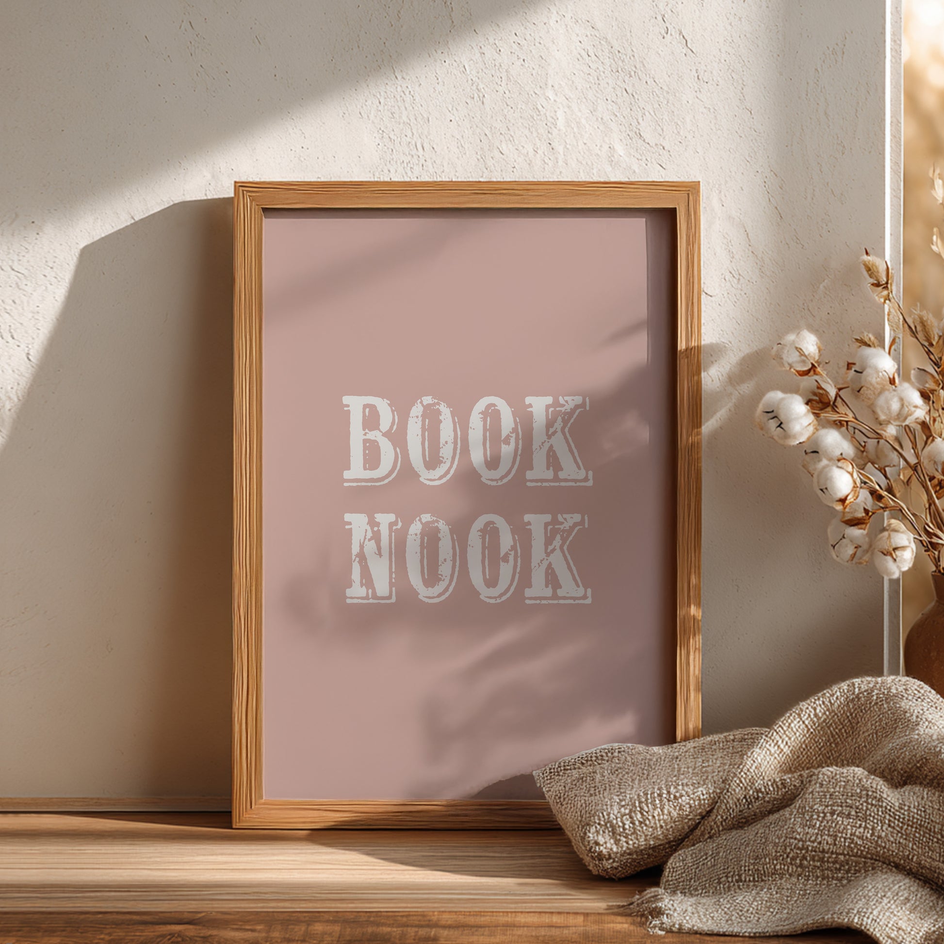 Wooden frame with 'BOOK NOOK' text on a pink background, placed on a wooden surface with decorative elements.