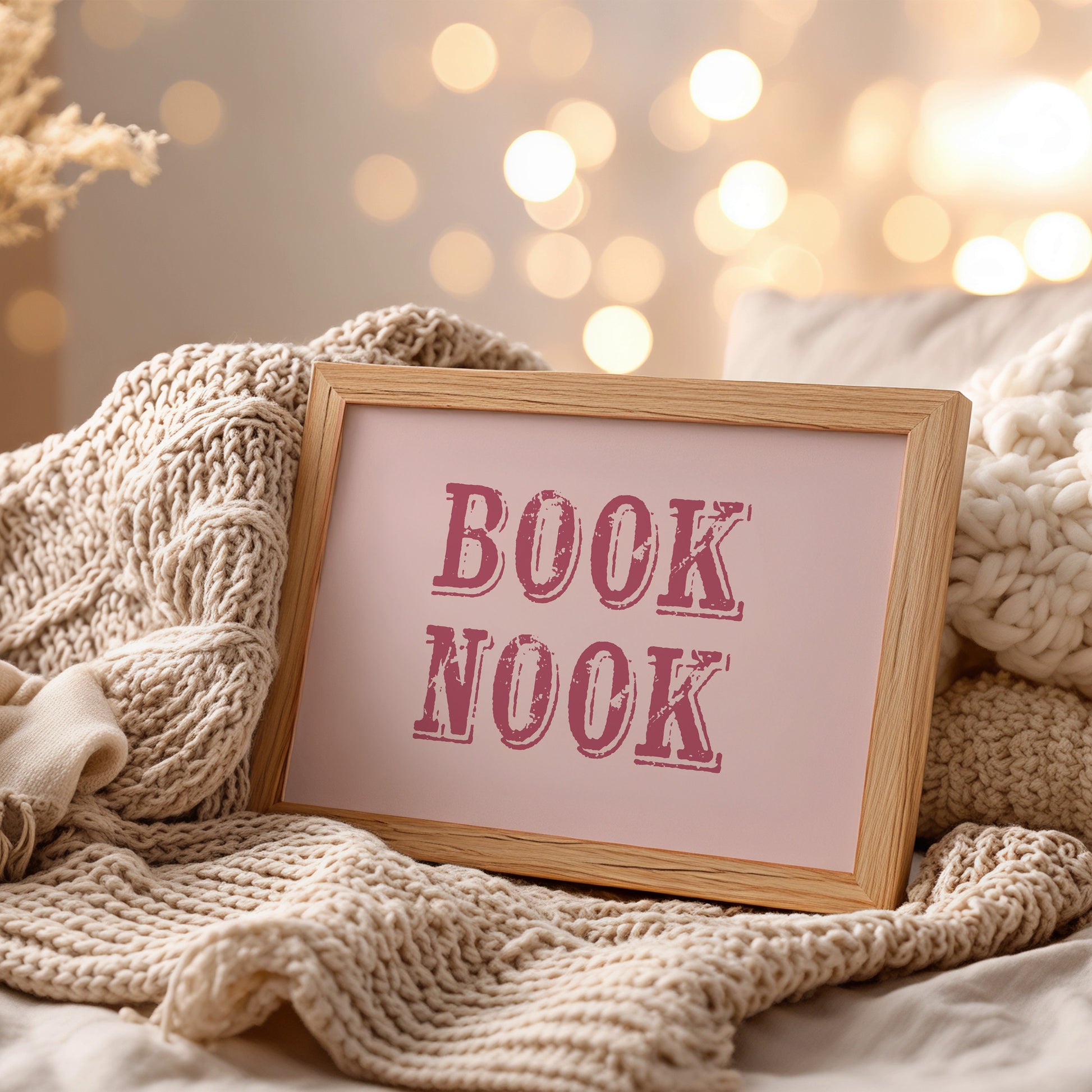 Framed wall art with 'BOOK NOOK' text on a cozy blanket with blurred lights in the background